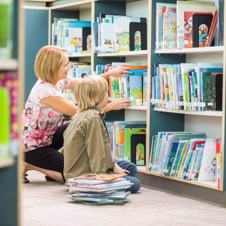 Frau mit Kind in einer Bibliothek zwischen Bücherregalen.