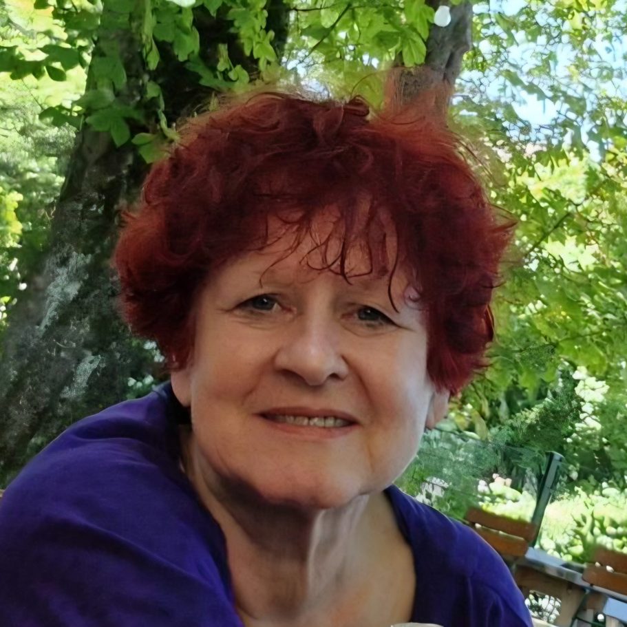 Frau mit lockigem Haar, Brille und freundlichem Lächeln, trägt ein rotes T-Shirt.