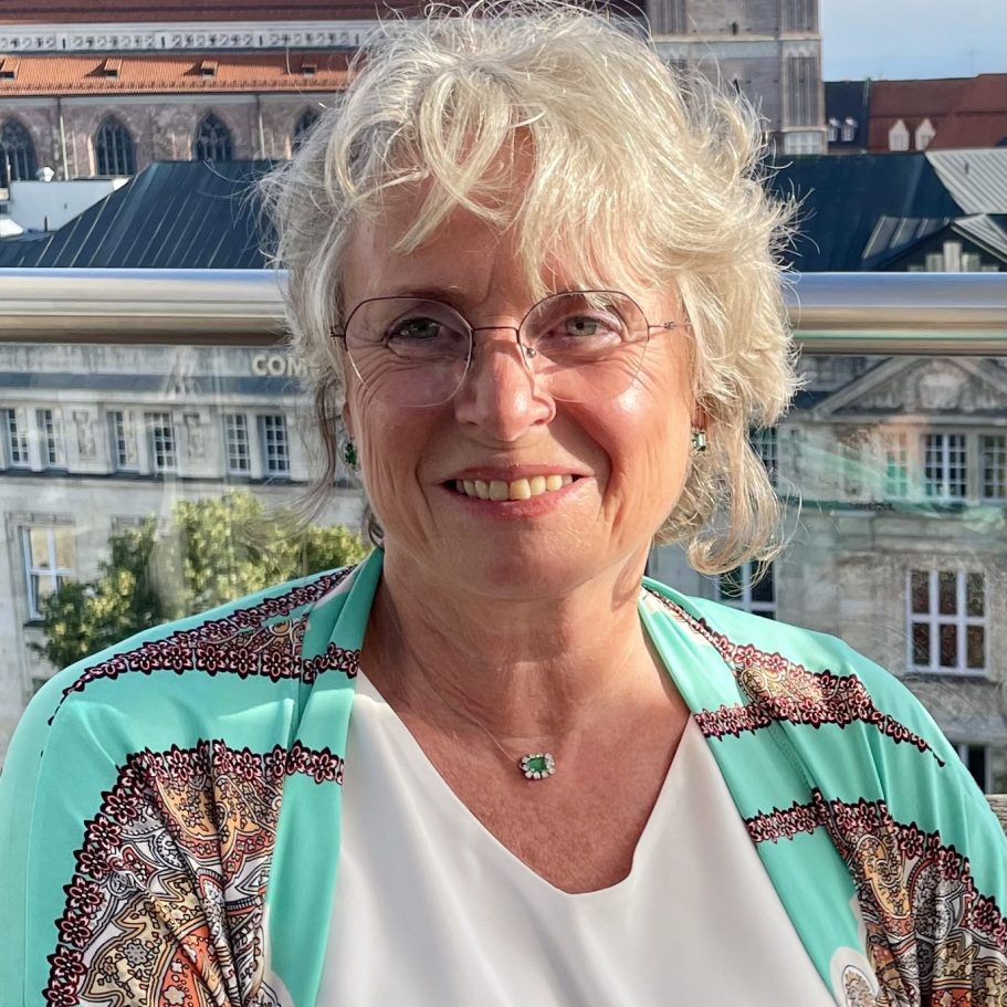 Lächelnder Mann mit Bart und buntem Weste, vor einem neutralen Hintergrund.