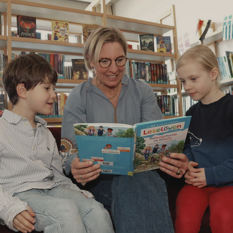 Junge und Frau lesen gemeinsam ein Buch in einer Bibliothek.