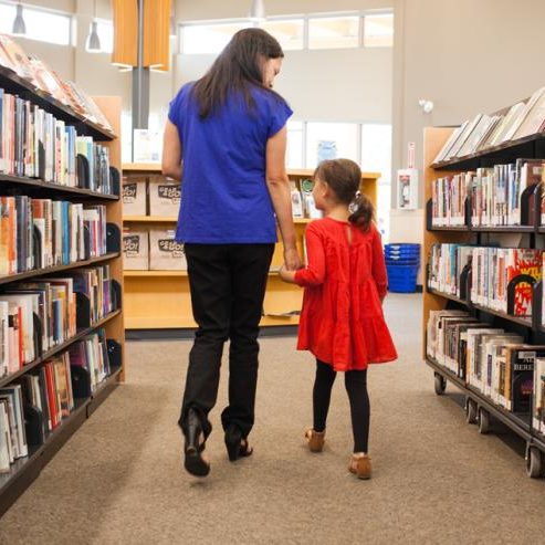 Frau mit Kind in einer Bibliothek zwischen Bücherregalen.